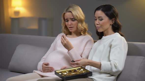 Woman Sitting With Upset Pregnant Friend, Eating Chocolate Candies, Hormones