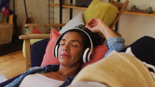 Caucasian woman listening to music with headphones on, lying on sofa at home