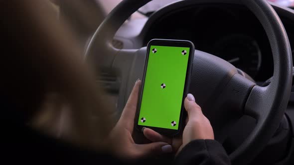 A Woman is Driving a Car with a Phone in Her Hands a Chroma Key on the Screen