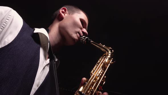 A Young Retro Stylish Guy Plays on the Golden Shiny Saxophone on Stage. Dark Studio with Smoke and