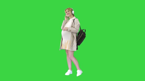 Pregnant Woman Standing and Listening Music in Headphones on a Green Screen, Chroma Key