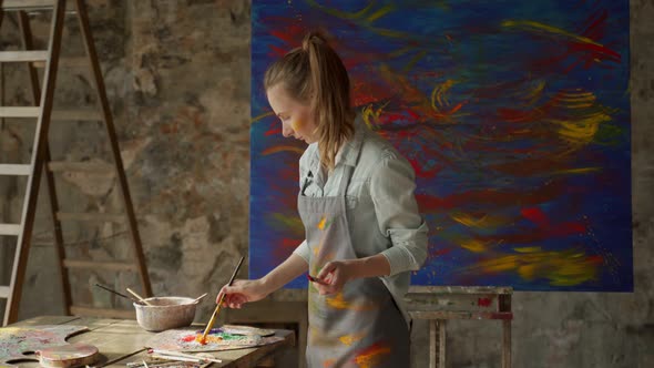 Woman Artist Holding Paint Brush on Large Canvas in Art Studio