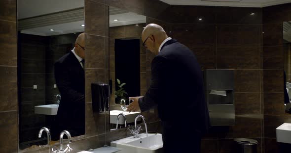 Successful Bald Man Is Washing Hands in Restroom of Hotel or Business Center