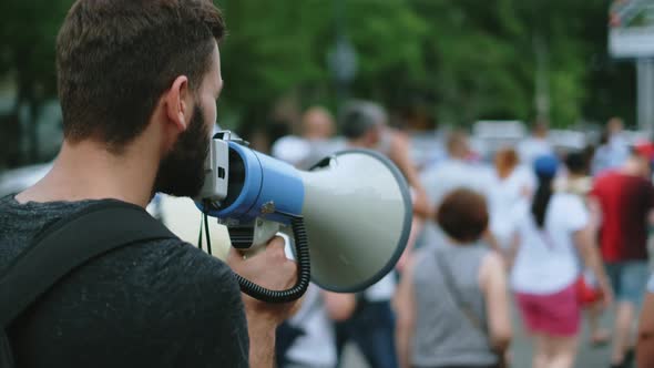 Young Bearded Male Protester with Megaphone Bullhorn Marches and Talks on Street