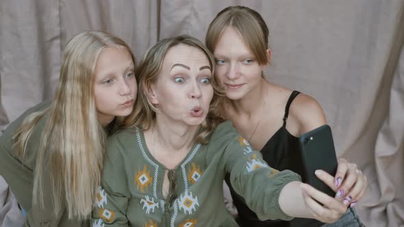 Close up of smiling mother with daughters makes funny selfies on the smartphone