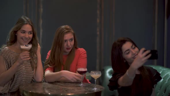 Three Cute Girls Sit in a Cafe or Restaurant Beautifully Posing and Taking a Photo Selfie for Social