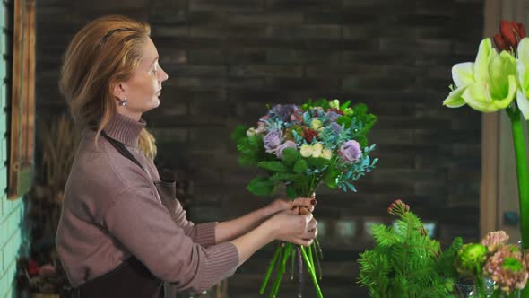 A Woman Florist in an Apron, Standing on the Counter in a Flower Shop, Preparing a Bouquet