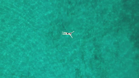 Top Down Aerial View of Woman Swims on Crystal Clear Water in a Transparent Sea