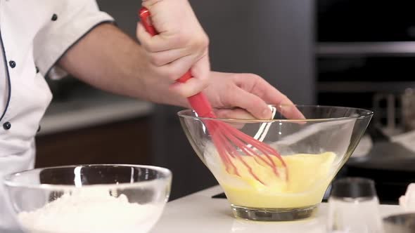 chef actively whips eggs in a transparent dish. Cooking an omelet in the kitchen