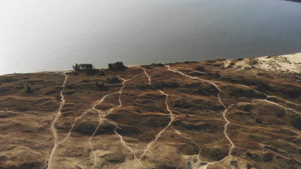 AERIAL: flying over the sand dunes paths towards the sea at the evening during golden hour