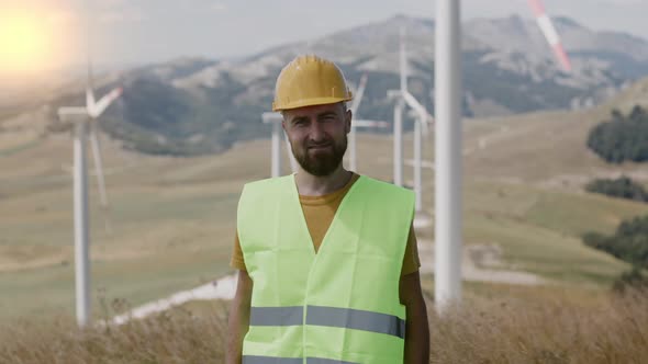 Portrait of Male engineer  in yellow hard hat and green uniform looking at camera Windmill Park