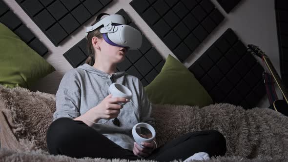 Young Woman in Virtual Reality Helmet Sitting on Sofa and Move Hands at Home