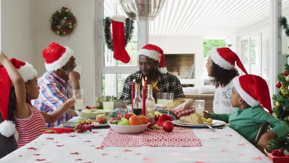 Happy african american multi generation family wearing santa hats and celebrating holiday meal