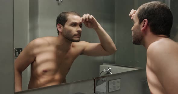 Young Man With Green Eyes Plucking His Eyebrows in Bathroom