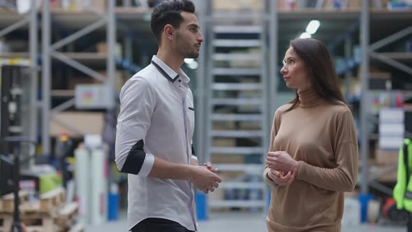 Young Middle Eastern Man and Caucasian Woman Talking Standing in Industrial Warehouse Indoors