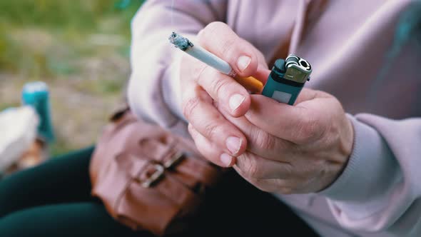 Woman Holding a Cigarette and a Lighter in Hands While Sitting in Nature on Sun