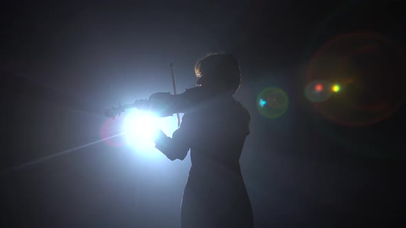 Girls Standing Back and Playing on Violins in a Dark Room. Black Smoke Background. Back View