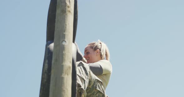 Smiling caucasian female soldier climbing down tyre wall on army obstacle course in the sun