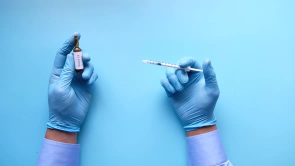 Hand in Latex Gloves Holding Glass Ampoule Vaccine and a Syringe on Blue