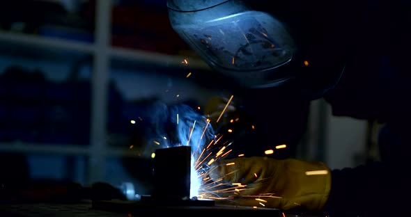 Worker in Mask Welds Details with Sparks and Smoke in Shop