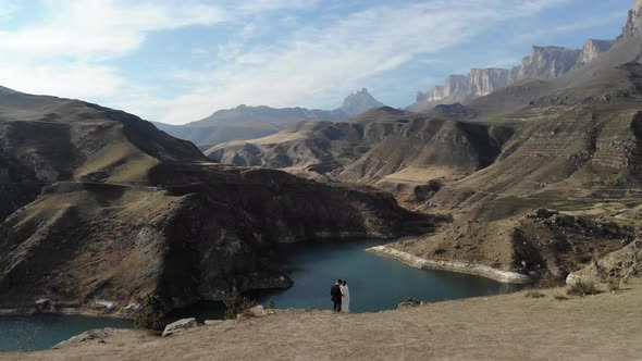 Aerial View From a Couple in Love Standing on the Edge of a Cliff Near the Water of a Mountain Lake