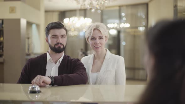Portrait of Confident Adult Caucasian Couple Talking with Receptionist in Hotel
