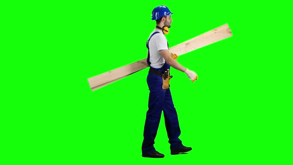 Builder in a Helmet Goes To Work with Wooden Boards in His Hands. Green Screen. Side View