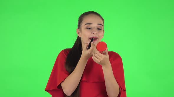 Portrait of Pretty Young Woman Is Painting Her Lips Looking in Red Mirror. Green Screen