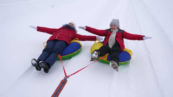 Happy Girls Sledding and Resting in Winter Park for Christmas Holidays