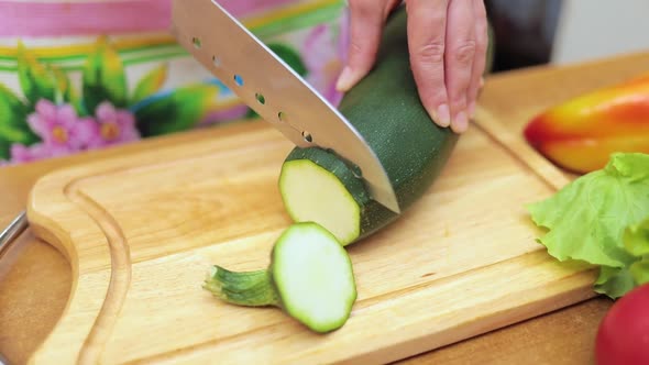 Women's Hands Housewives Cut with a Knife Fresh Zucchini on the Cutting Board of the Kitchen Table