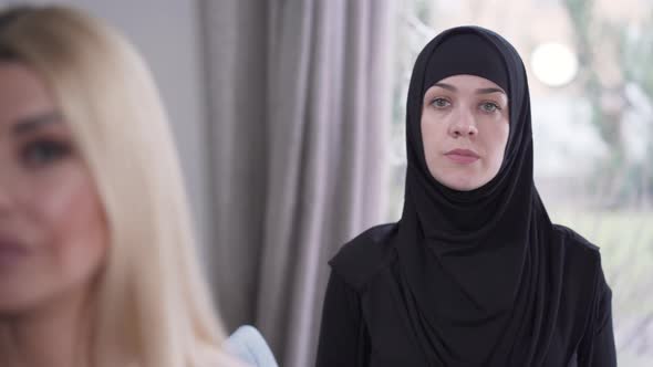 Focus Changes From Modest Muslim Woman in Hijab To Face of Young Modern Caucasian Lady Looking at