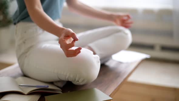 Close-up of Unrecognizable Young Woman Practicing Yoga While Sitting in Lotus Pose at Desk at Home.