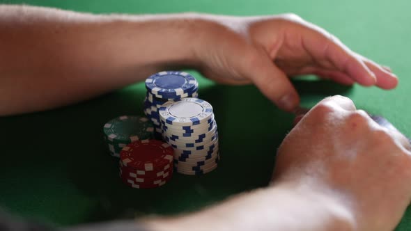 A man looking at his cards and guarding his poker chips. He has black jack twenty one pontoon with a