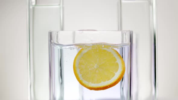 Slice of Lemon Falls Into the Water in a Glass Container on a White Background