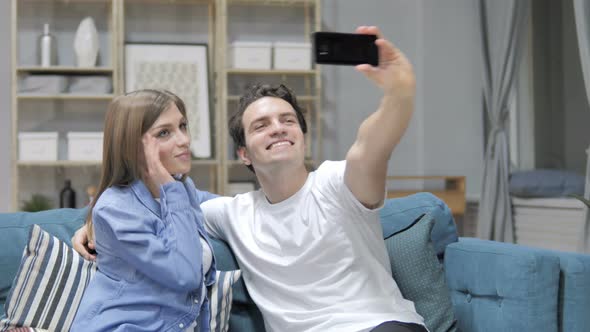 Young Couple Taking Selfie with Smartphone While Sitting on Couch