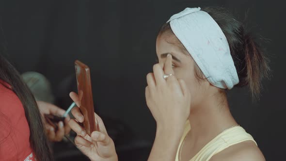 Beautiful young woman looking at the mobile camera to look how the make up artist make up her