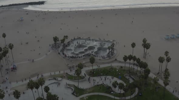AERIAL: Flying Towards Venice Beach Skatepark with Visitors and Palm Trees, Sunset, Los Angeles