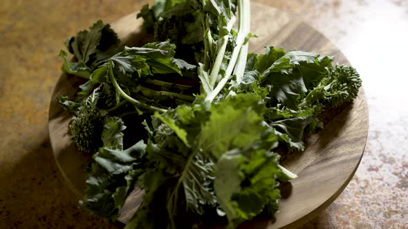 Clusters of stalks of fresh rapini on a round cutting board rotating in beautiful backlit light.