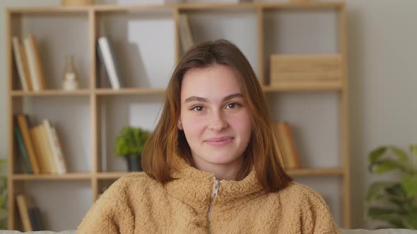 Happy Cute Positive Caucasian Brunette Young Woman Sitting on Sofa on Living Room Background Looking