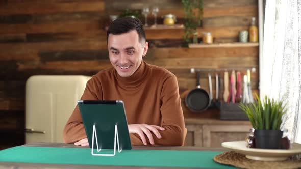 Young Cheerful Man Using Tablet Computer Having Online Video Chat with Friends.