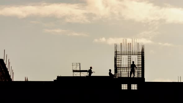 Silhouette of Workers Working with Steel Rebar on Construction Site, Sunny Evening, Golden Hour