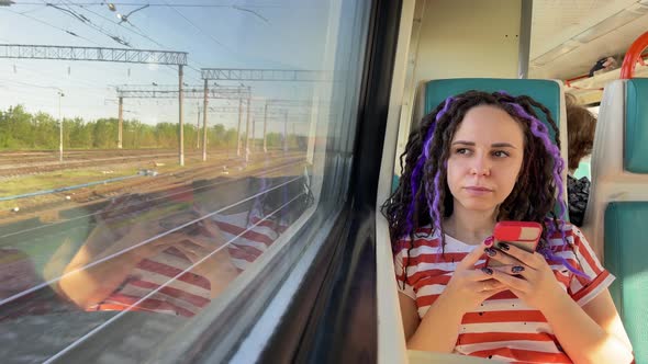 Young thoughtful woman with mobile phone riding on train.