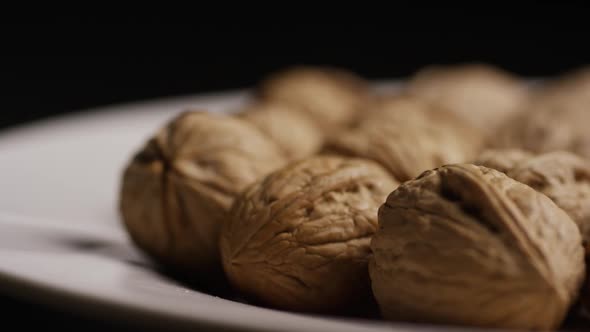 Cinematic, rotating shot of walnuts in their shells on a white surface 