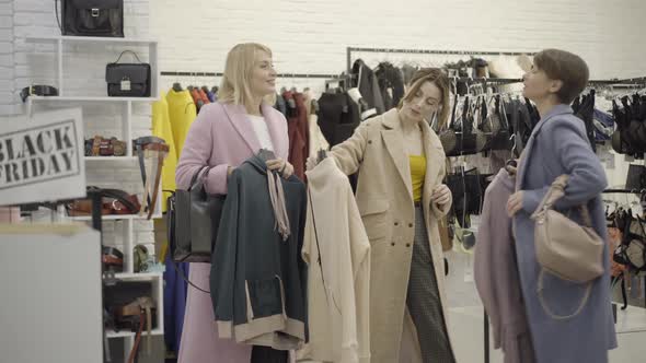 Wide Shot of Three Confident Shoppers Choosing Pricey Clothes in Shop During Black Friday Sales