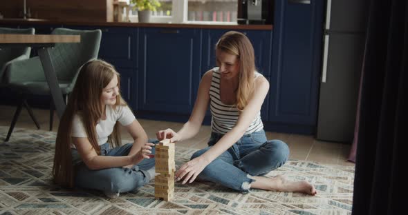 Mother and Daughter Build Tower From Wooden Bricks Sitting on a Floor at Home