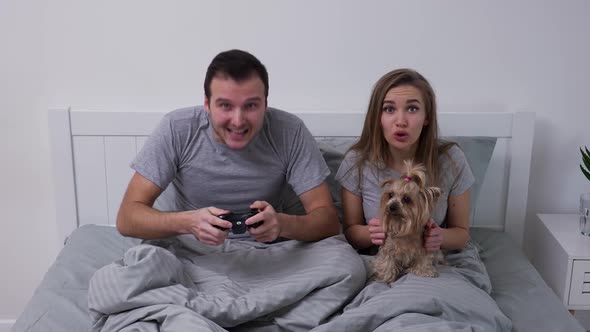 Happy Young Couple Lies in Bed with Small Dog