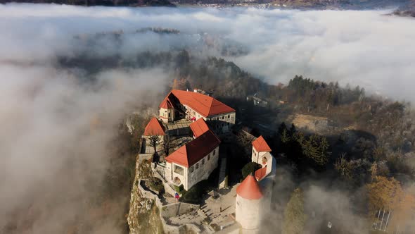 Bled castle illuminated by morning golden hour light; above low clouds