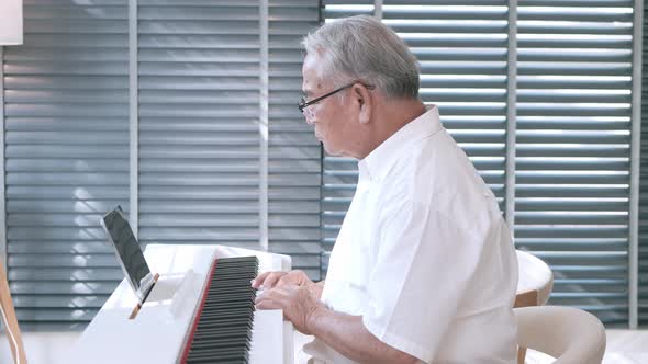 Senior Asian man learning to play chirping with the help of a virtual class.