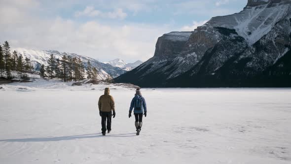 The Incredible Ice Lake in Rocky Mountains with Tourist Couple Hikers Walking Away to Beautiful Scen