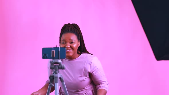 Dark Skinned Woman Laughing and Shooting Social Media Stories in Pink Wall Background